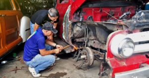 In a garage, two men are working together on an old truck, focused on repairs.